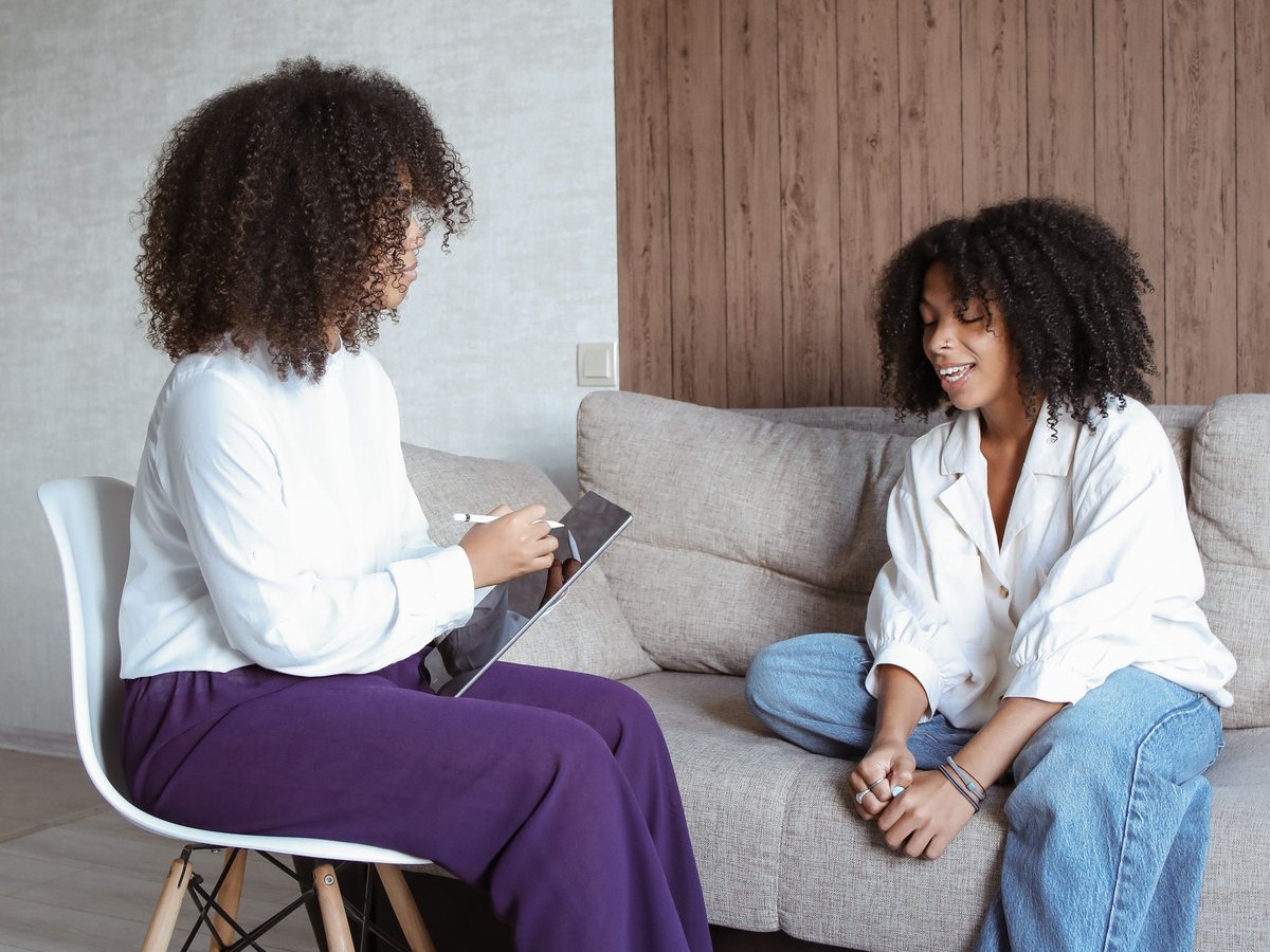 A coaching session in progress — two women talking across a table with notebooks and coffee