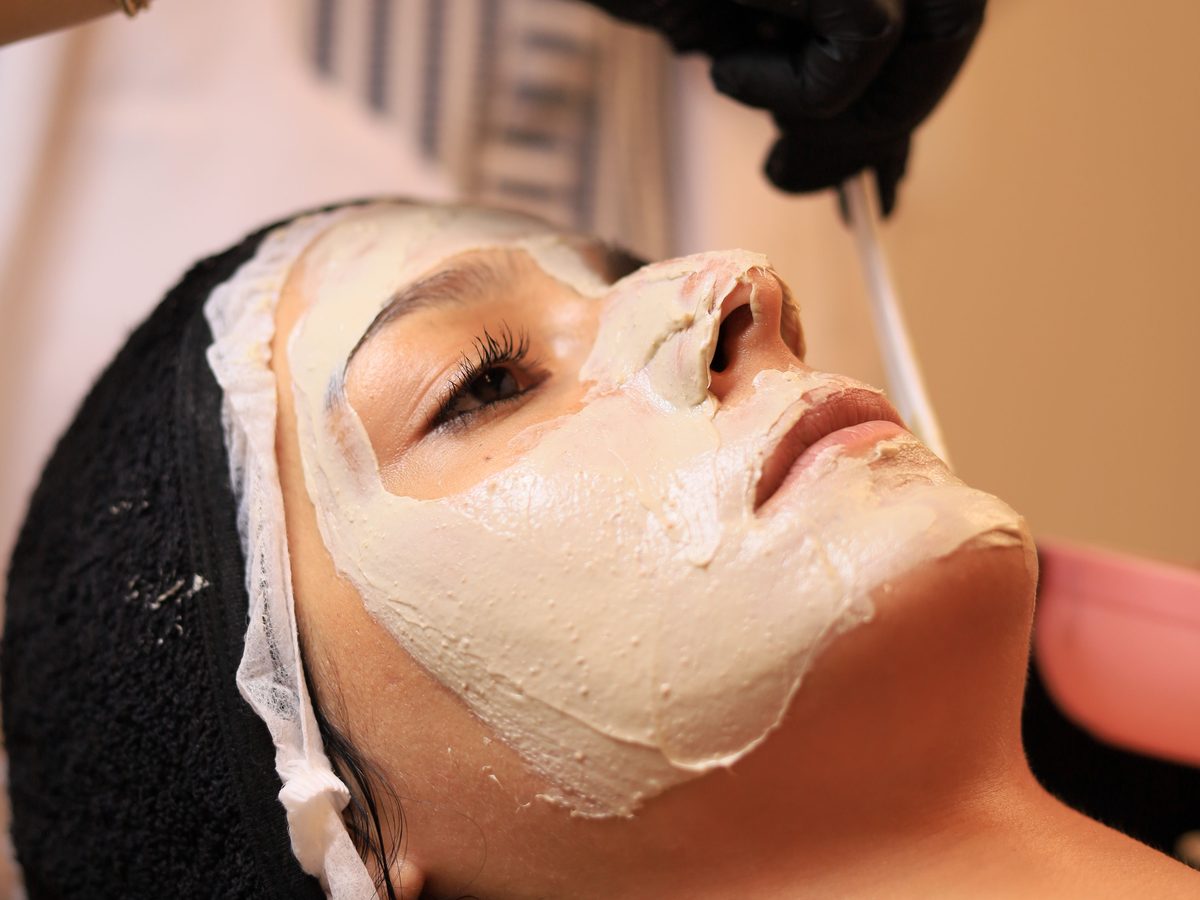 An esthetician working through a facial, warm towel and mask on the treatment table